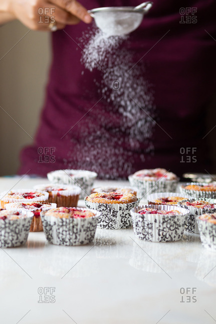 View of woman sprinkling fresh gluten free strawberry muffins with confectioners sugar