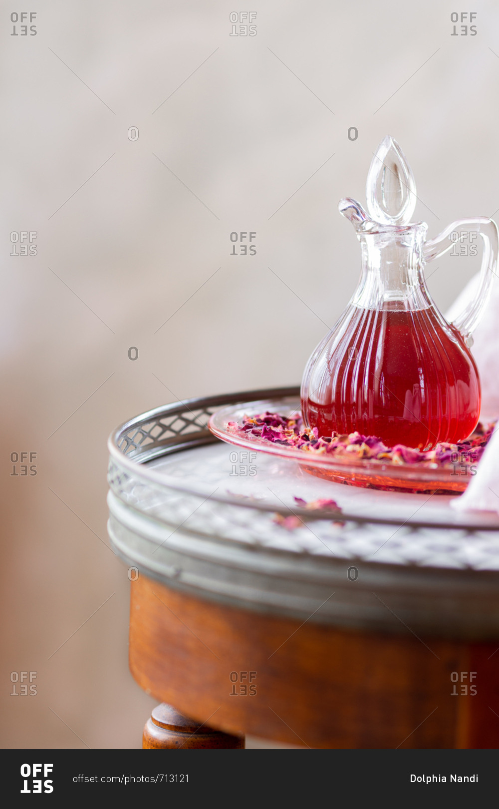 Glass server of rose syrup arranged with rose petals on marble table