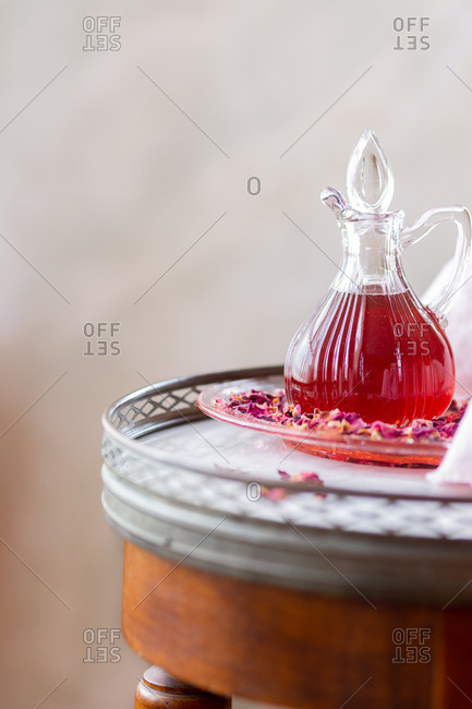 Glass server of rose syrup arranged with rose petals on marble table