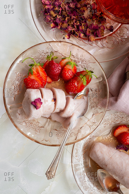 Overhead view of bowl of melting kulfi and sliced strawberries served with rose syrup