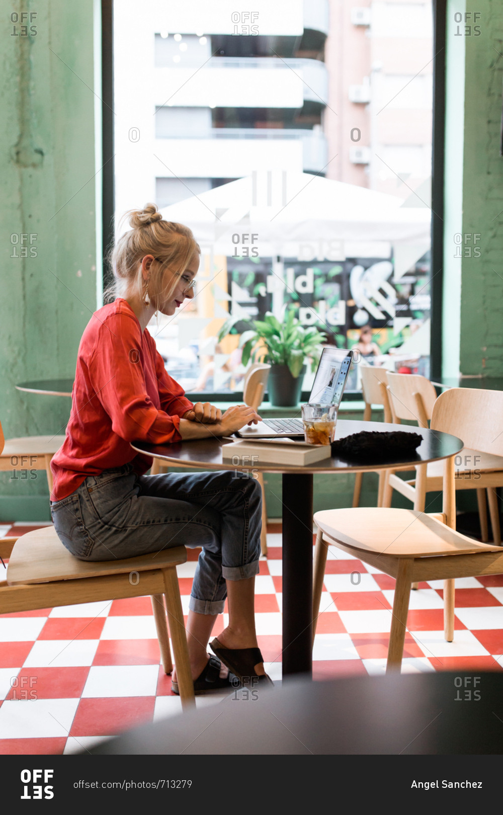 Young vintage girl with a red shirt working with her laptop in a coffee bar in the afternoon