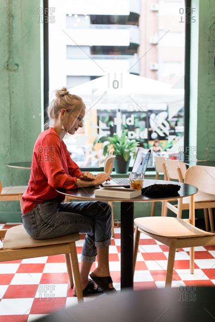 Young vintage girl with a red shirt working with her laptop in a coffee bar in the afternoon
