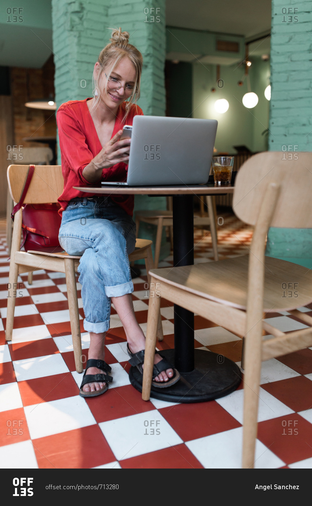 Vintage blonde girl with a bow and red shirt using her phone while smile in a coffee bar
