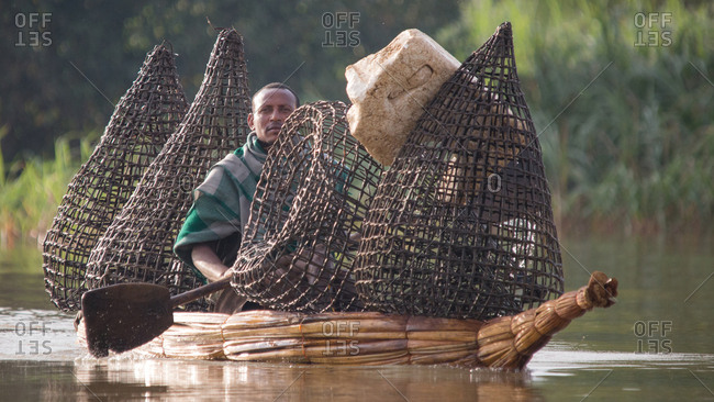 Ethiopia - November, 25, 2014: Male rowing canoe with cages for fish by paddle at river