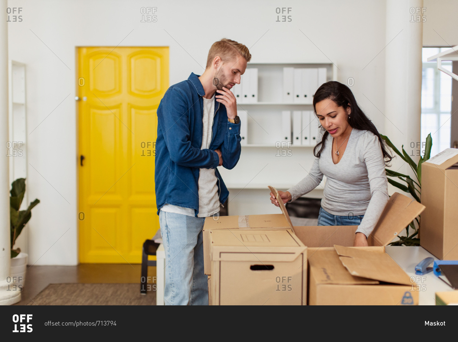 Young businessman looking at businesswoman opening cardboard box at office