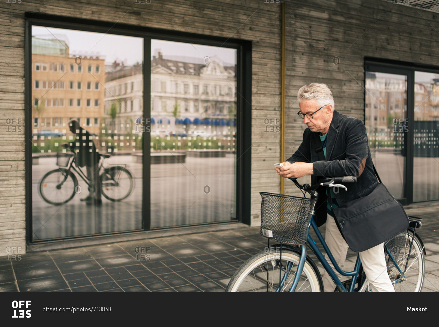 Senior man using smart phone while standing with bicycle against building in city