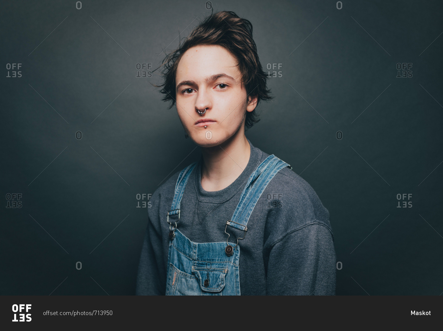 Portrait of trendy young man wearing bib overalls over colored background