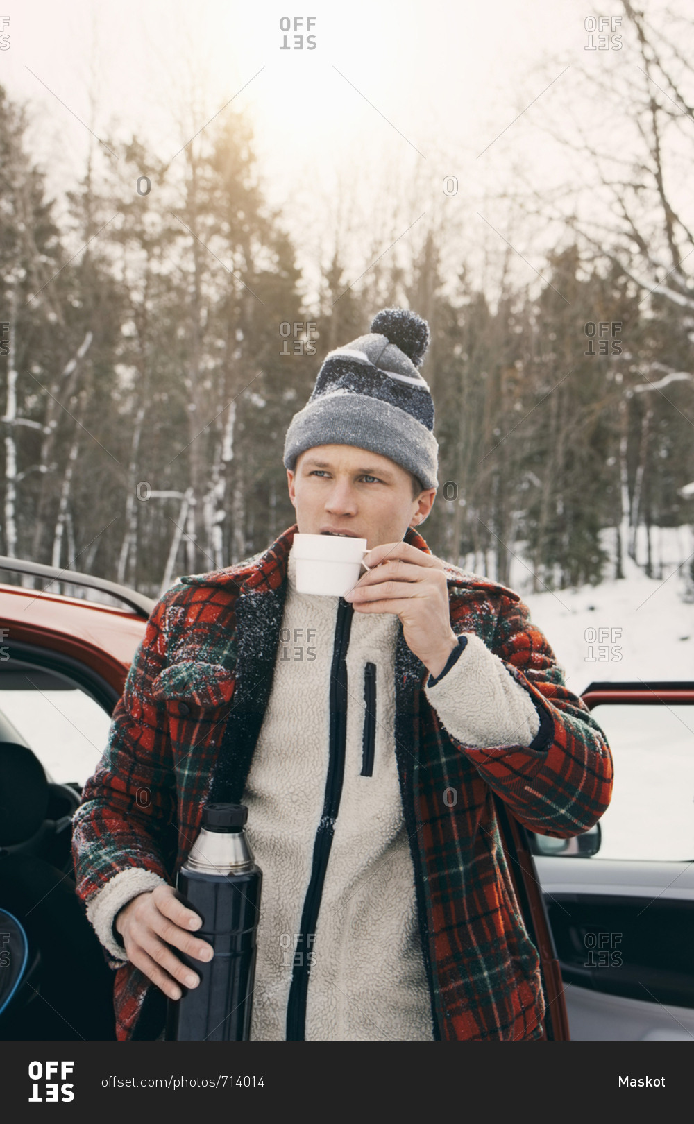 Man drinking coffee from insulated drink container while standing by car at park