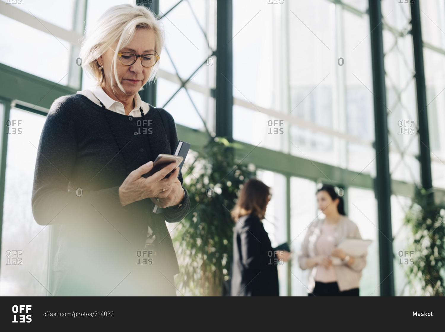 Senior businesswoman using mobile phone while colleagues communicating in background