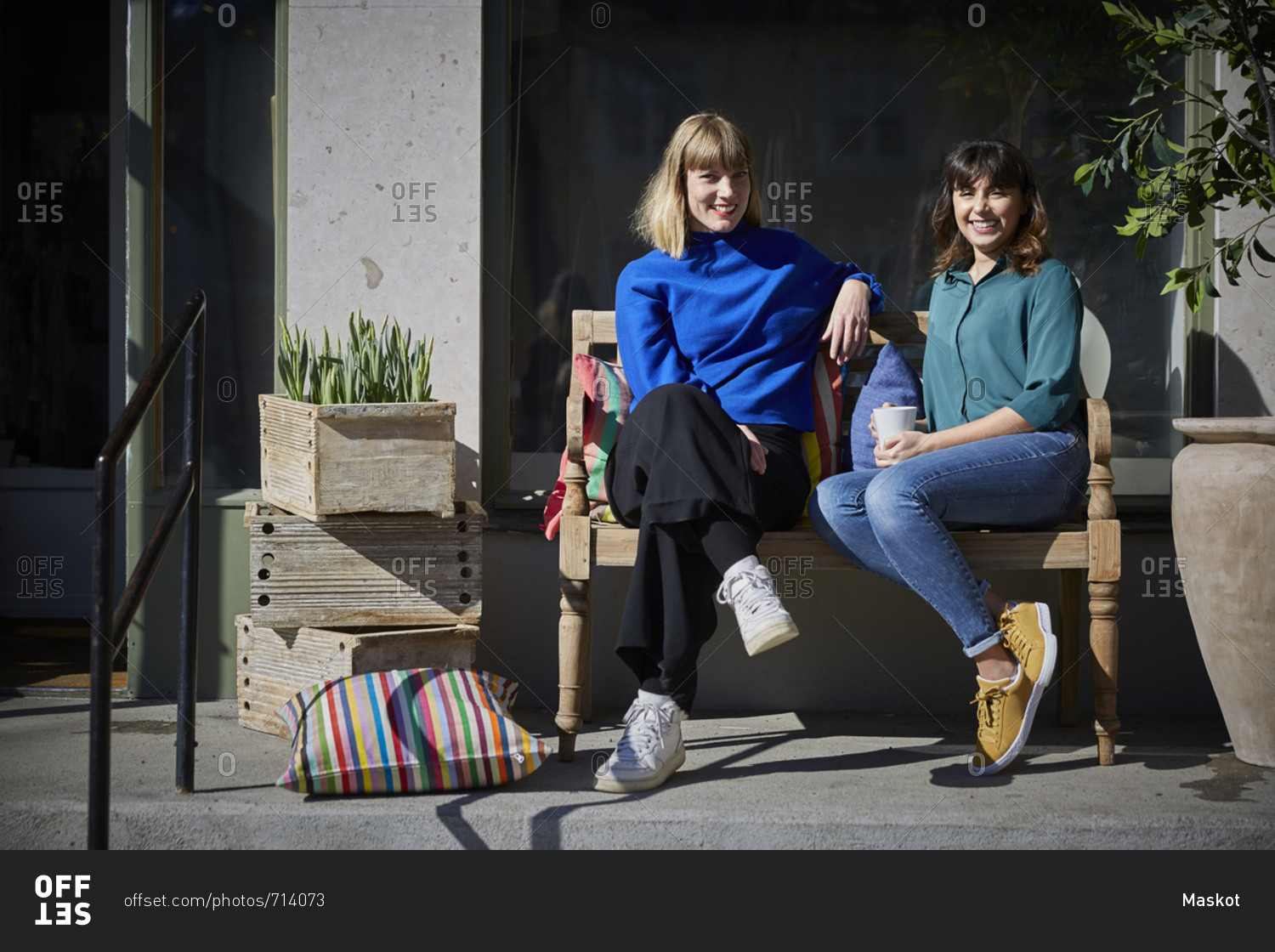 Full length portrait of smiling owners sitting on bench outside store