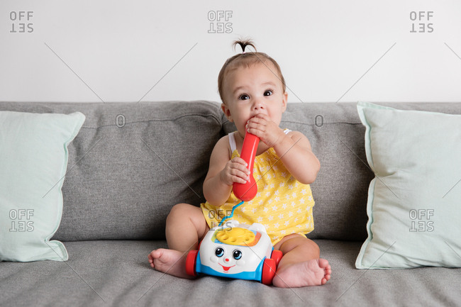 Baby girl sitting on sofa chewing on toy phone