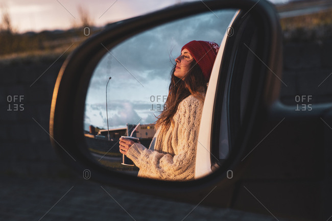 Iceland- young woman with coffee to go at sunset- mirrored in wing mirror