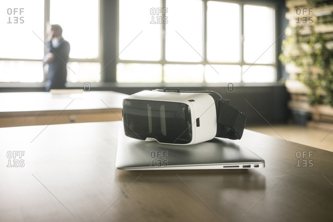 VR glasses and laptop on table in office with businessman in background