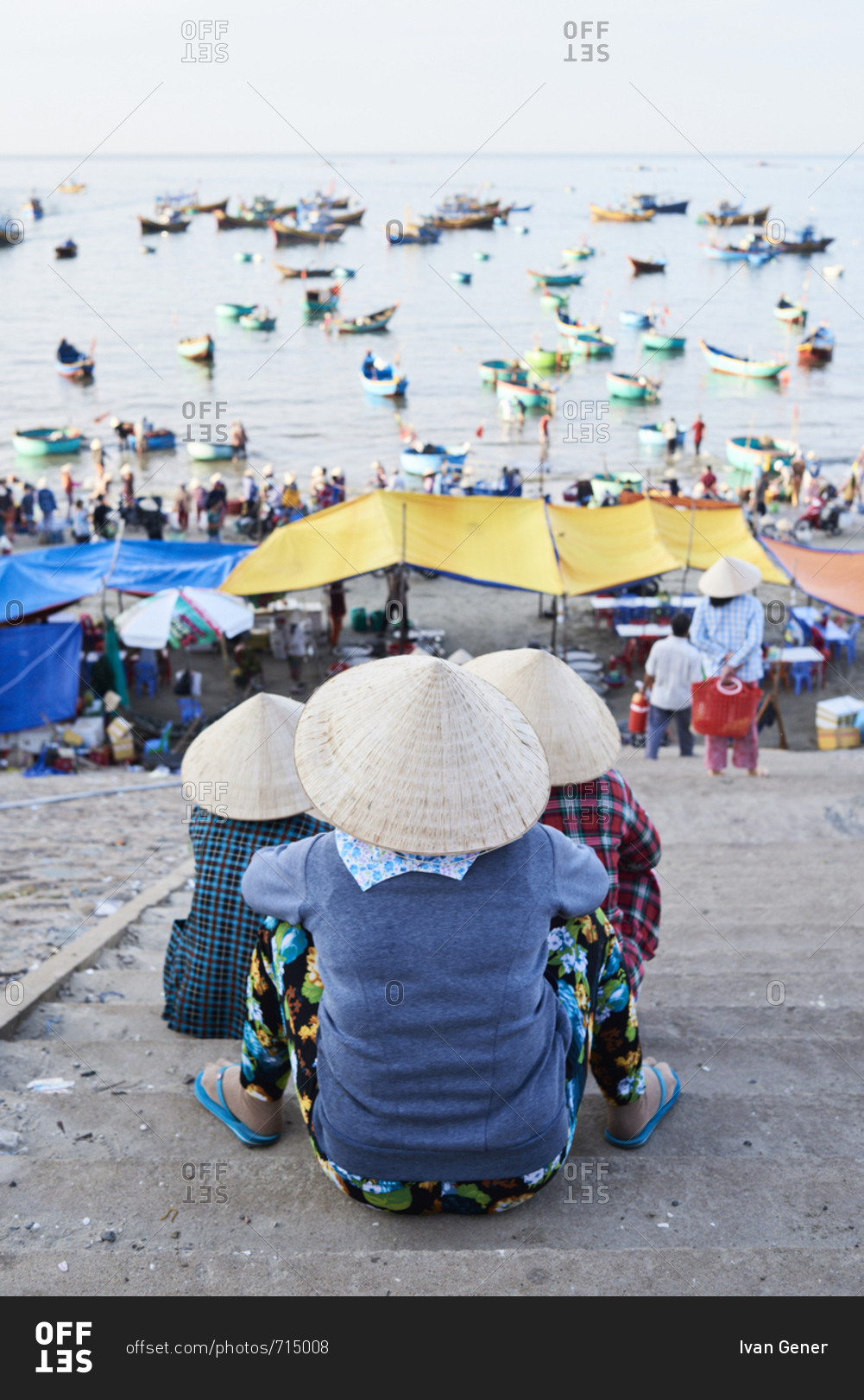 Three faceless senior women observing activity at Mui Ne fishing market at early morning when fishers arrive to harbor with seafood and fish goods
