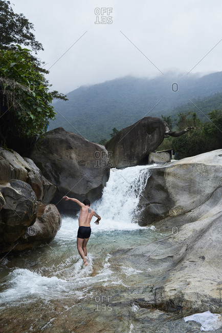 Faceless male adventurer walking in natural slip and slide waterfall in summer