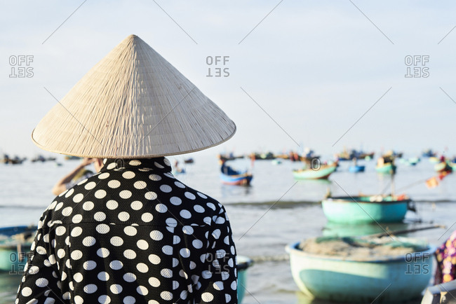 Faceless vietnamese woman wearing hat watching activity at seashore of fishing market