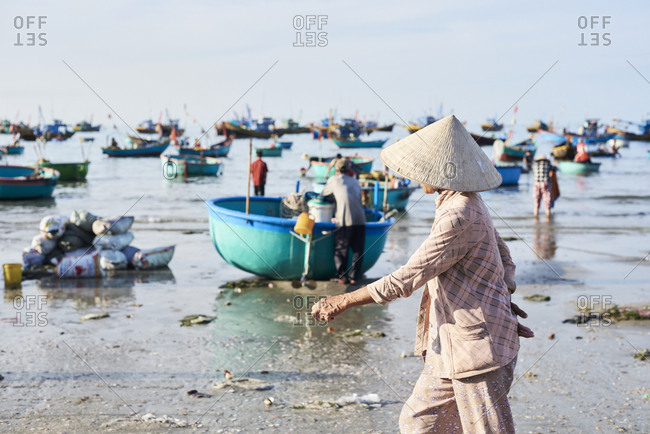 Faceless vietnamese woman wearing hat walking around seashore while supervising activity at clandestine fishing market