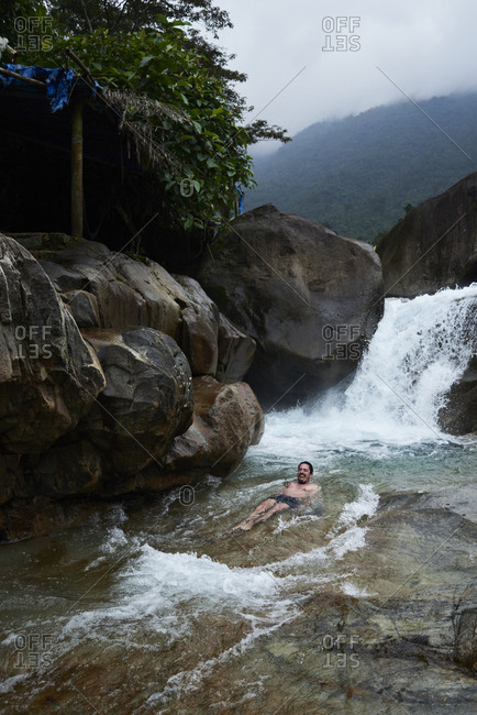 Brunette happy adventurer enjoying the fall down in natural slip and slide waterfall in summer