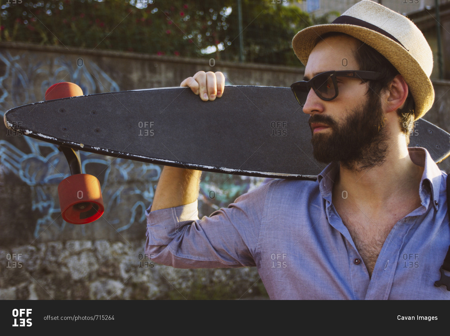 Man wearing sunglasses and hat while holding skateboard against wall