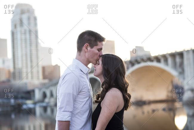 Husband kissing on pregnant wifes forehead while standing by river against clear sky in city stock photo photo