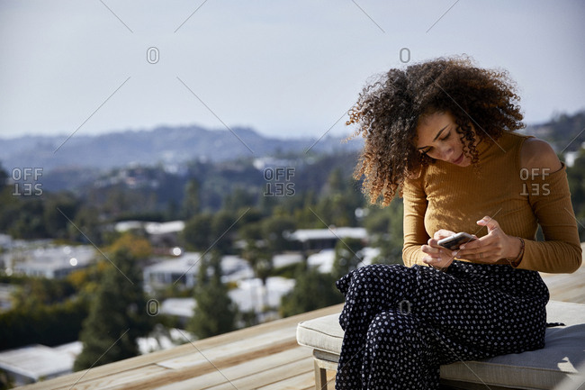 Woman using mobile phone while sitting on deckchair against sky