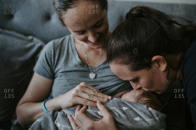 Close-up of lesbian mothers with newborn son sitting on bed at home