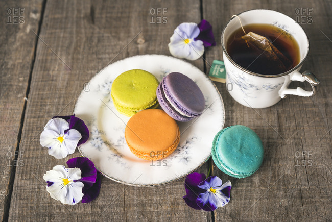 High angle view of tea with colorful macaroons and flowers served on wooden table