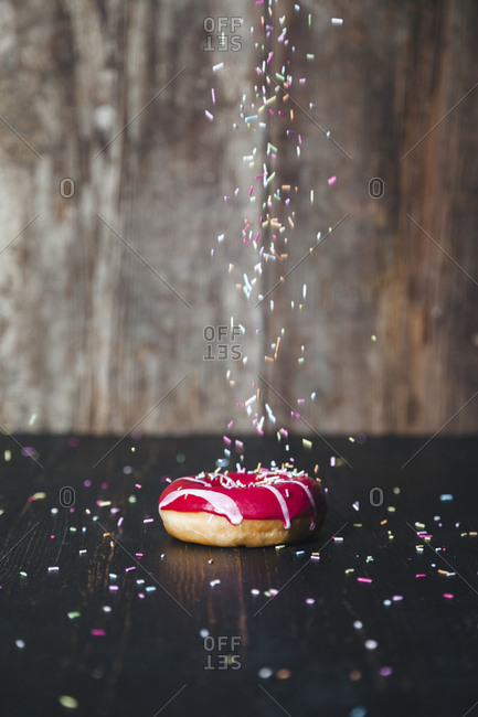 Sprinkles sprinkling on donut at wooden table