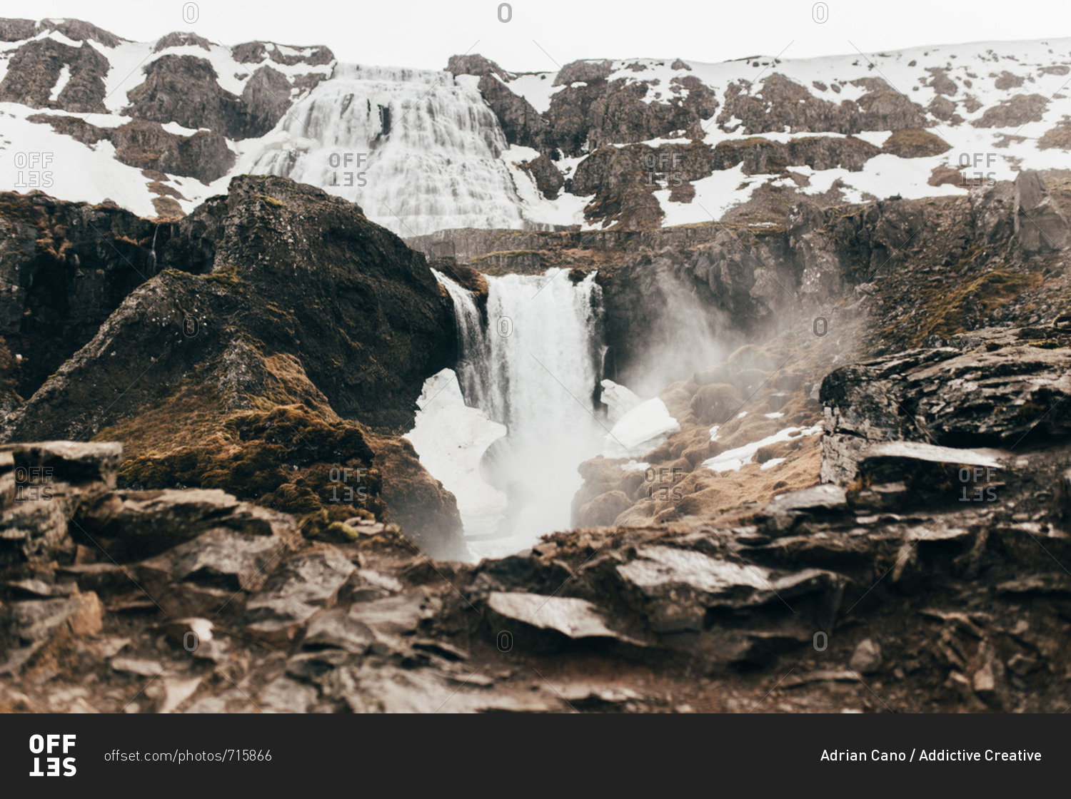 Landscape of waterfall flowing among rocks and snow from high mountain in mist, Iceland.