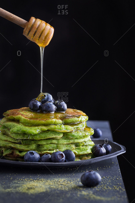 Honey pouring from wooden spoon to tasty green pancakes with blueberry.