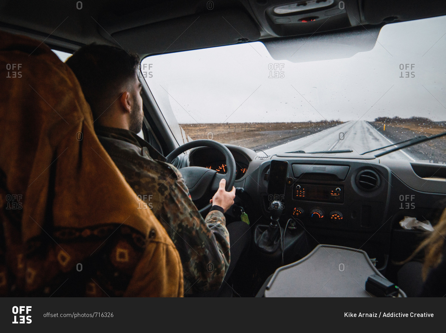 Back view of man driving car down remote road in plains of Iceland in rainy and gloomy day.