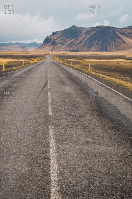 View of long paved road running far away on plain with high mountains on background, Iceland.