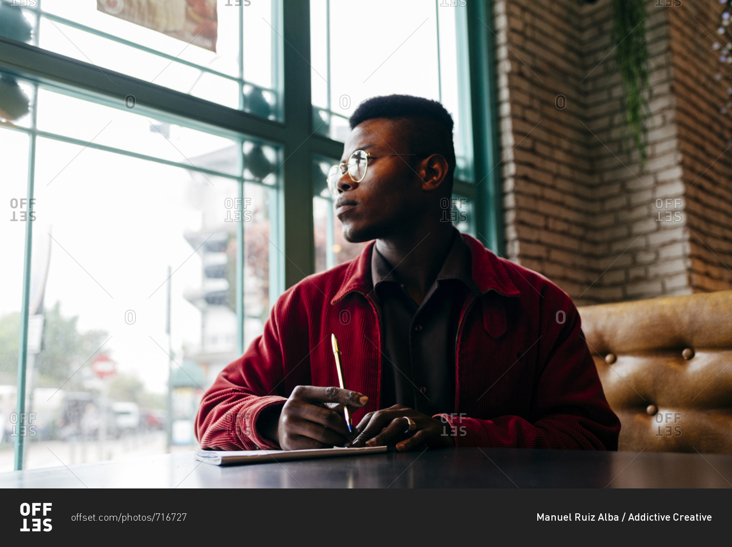 Serious african male in red jacket letter at table in cafe