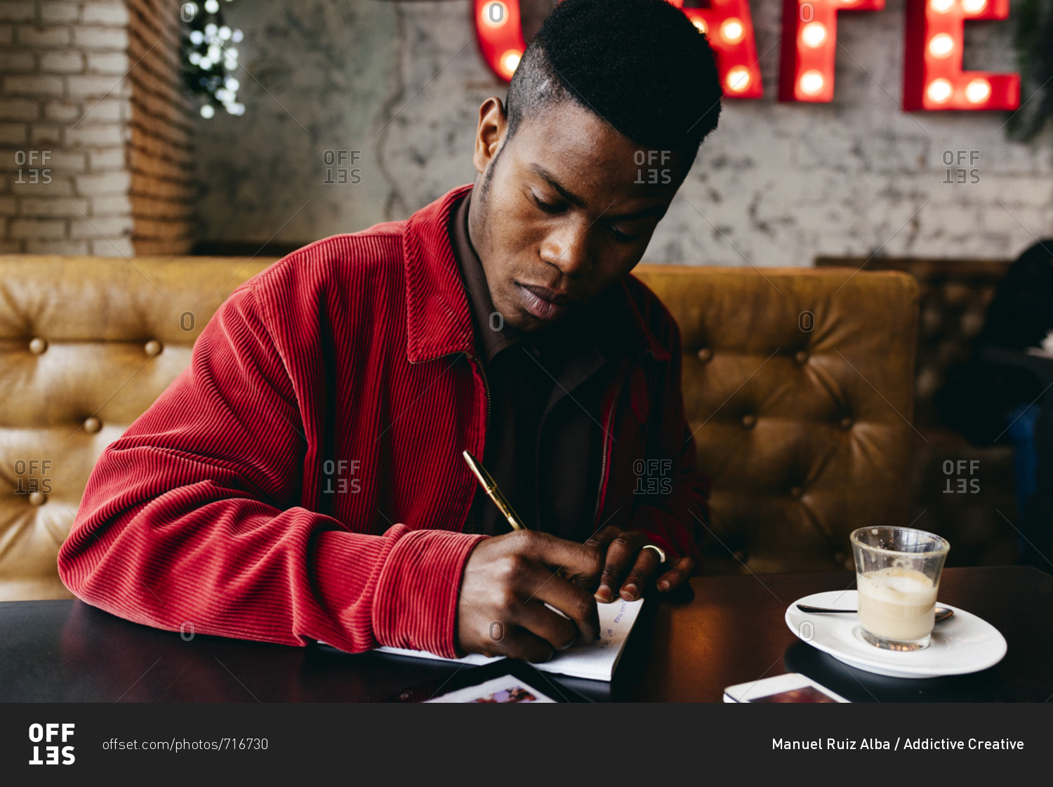 Serious african male in red jacket letter at table in cafe