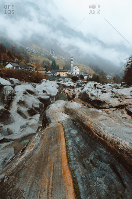 Small river and wet stones at the town placed in mountains in foggy day.