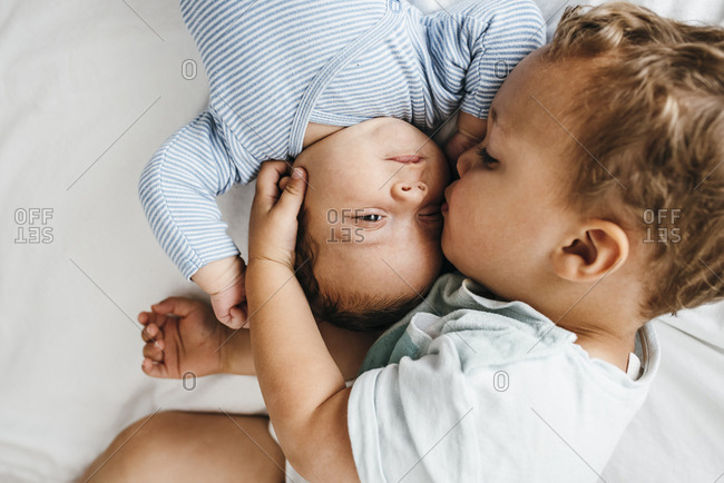 Young boy kisses his baby brother in bed