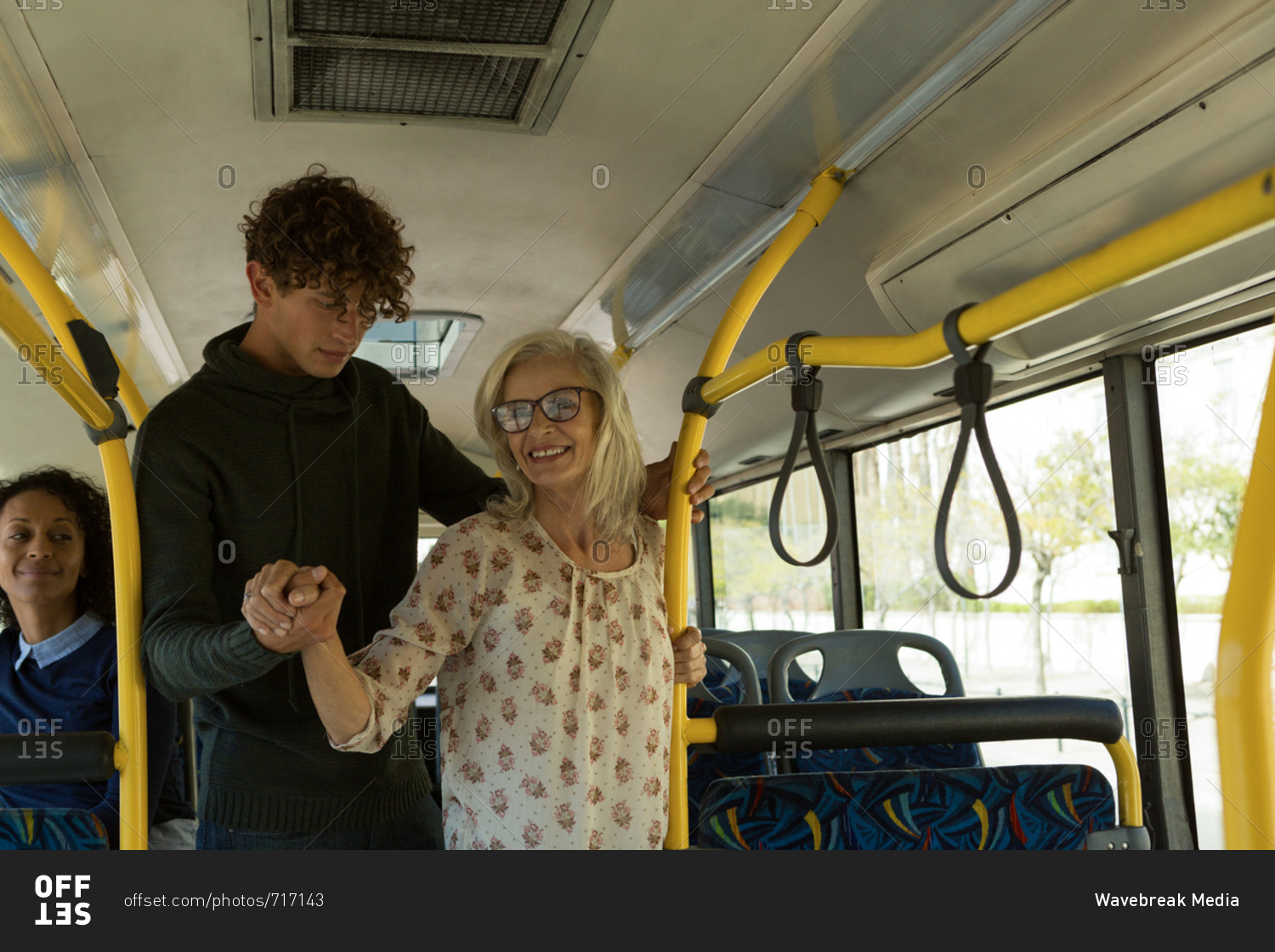 Young man helping senior woman while travelling in the bus