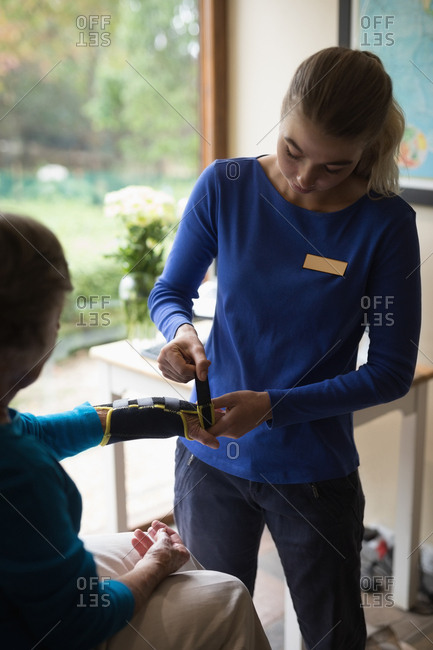 Physiotherapist putting on a wrist support brace on senior woman at home