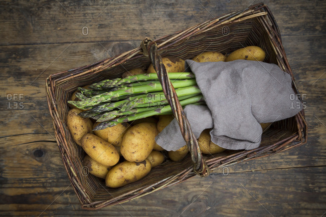 Organic green asparagus and organic potatoes in wickerbasket on wood