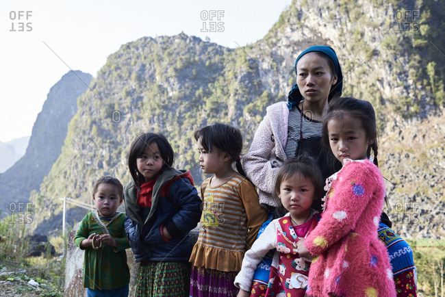 Ha Giang, Vietnam - February 16, 2018: Family photo of mother looking away surrounded by her children against rocky landscape.