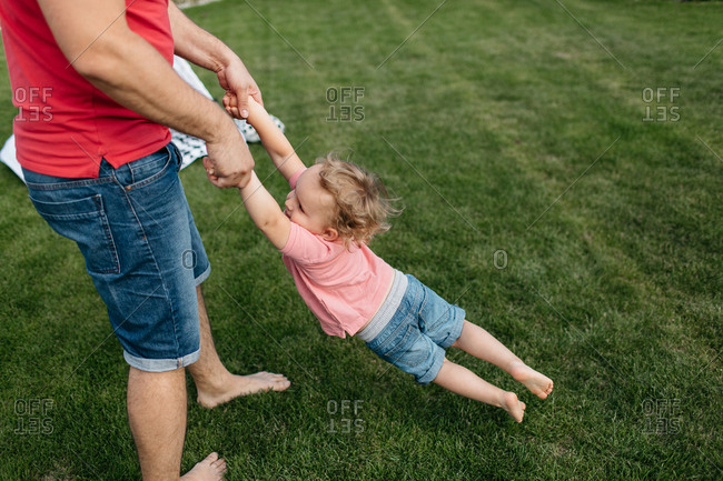 Father spinning his little son outside in the garden. Happy child having fun with his father.