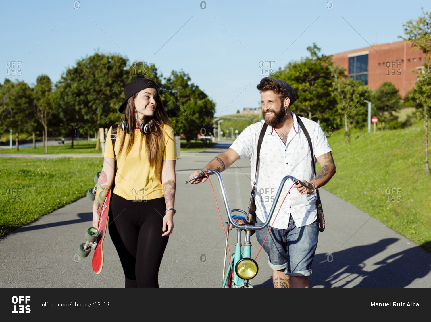 Trendy couple with tattoos walking on the street with a skateboard and a vintage bicycle