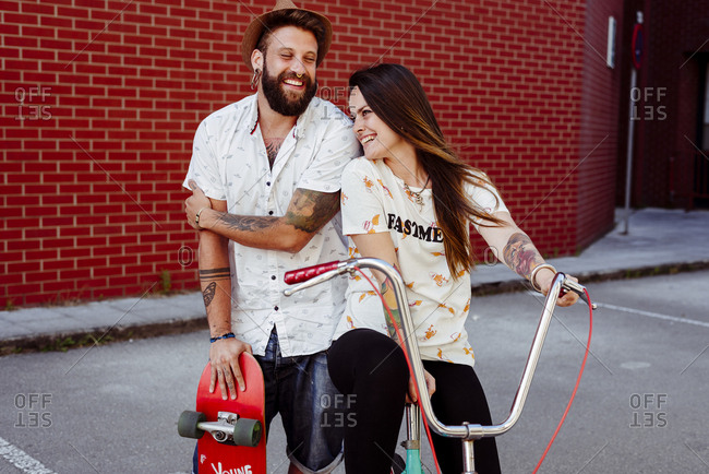 Trendy couple with tattoos standing on the street with skateboard and vintage bicycle