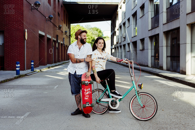 Trendy couple with tattoos standing on the street with skateboard and vintage bicycle