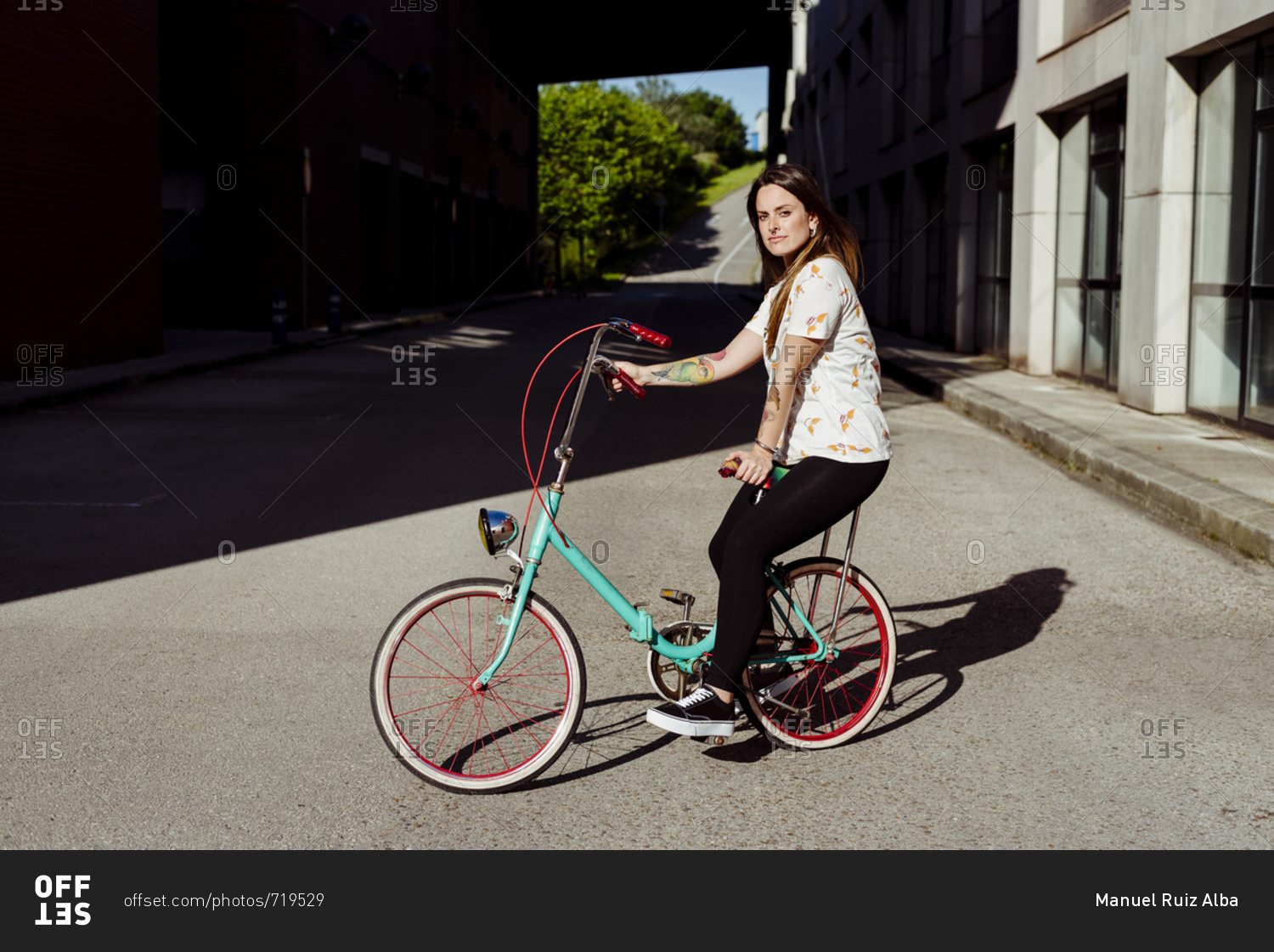 Trendy tattooed woman sitting on a vintage bicycle in the middle of the street
