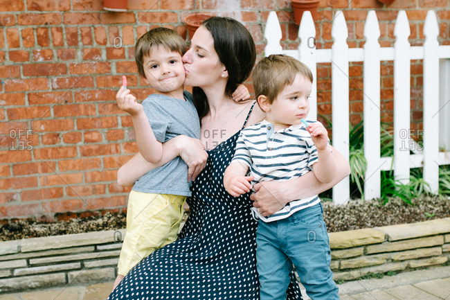 Mother kissing boy's cheek while embracing two sons