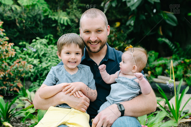 Father holding son and daughter in a botanical garden
