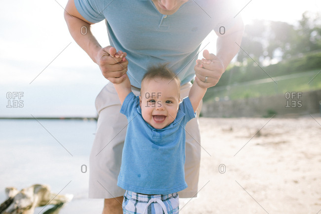 Happy baby holding parents hands on a beach
