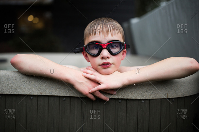 Boy wearing swim goggles resting head on arms at edge of swimming pool