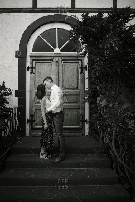 Engaged couple kissing on steps at front entrance to house